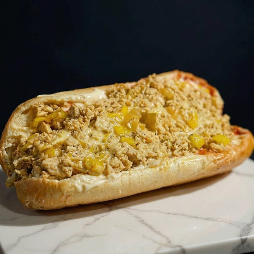 A large, open-faced sub sandwich filled with chicken, yellow peppers, and creamy sauce.